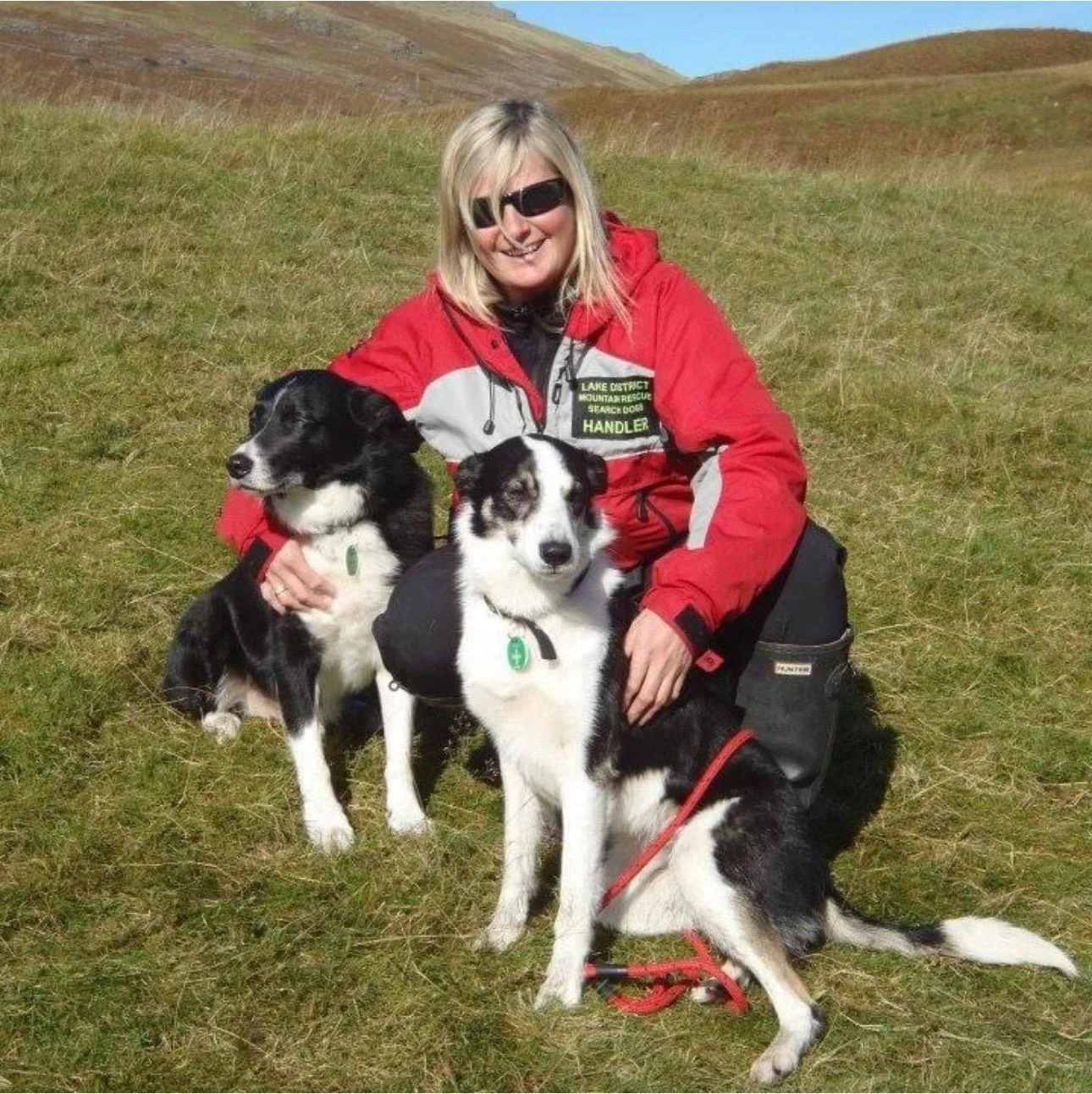 Christyne sitting on a grassy fell with three dogs